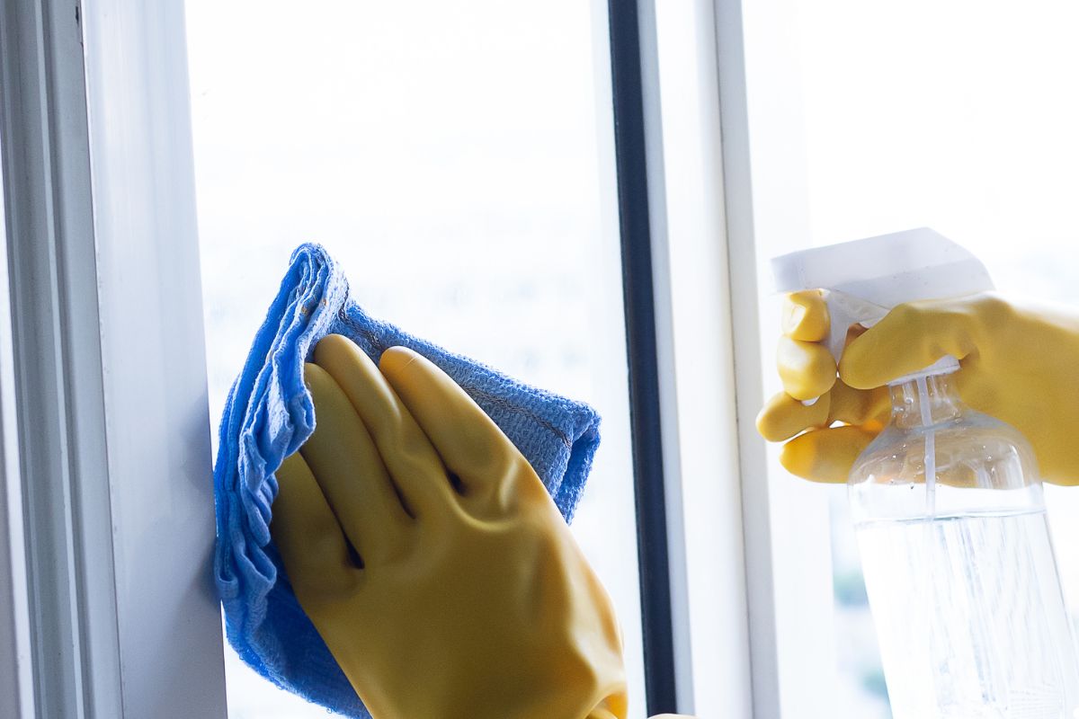 A person wearing rubber gloves is cleaning a window with a cloth, focusing on removing dirt and streaks.